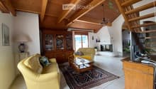 Living room with exposed wooden beams, cream-colored sofas, coffee table, cabinet, table lamp, television, fireplace, and chandelier.