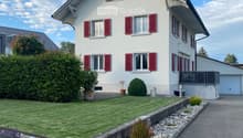 Two-story house with white walls, red shutters, and a well-maintained garden with a gravel pathway.