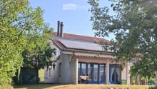 Two-story house with a red-tiled roof, solar panels, large windows, and a covered patio area with outdoor furniture.