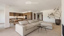 Modern living and dining area with a large sectional sofa, coffee table, dining table with chairs, and a kitchen area with wooden cabinets and appliances.