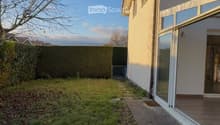 Backyard with a concrete pathway leading to a house entrance, surrounded by a hedge and sparse grass.