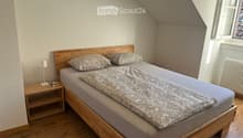 Cozy attic bedroom with wooden bed, nightstand, lamp, and radiator. The bed has a grey duvet and patterned pillows.