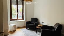 A room with two armchairs, a coffee table, a carpet, a floor lamp, and a window with view to outside.