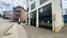 Modern building with large glass windows and a private entrance sign, located on a paved sidewalk next to a street with other buildings and a parked car.