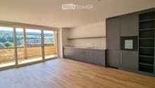 Modern kitchen with grey cabinets, wooden flooring, and large sliding glass doors leading to a balcony with a scenic view.