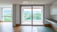 Bright, unfurnished room with wooden flooring, large windows, and a sliding glass door leading to a balcony with scenic views.