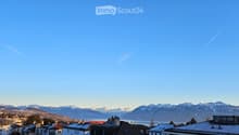 Panoramic view of a town with snow-capped mountains and a lake in the background under a clear blue sky.