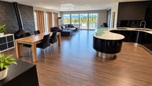 Open-plan living and dining area with modern furniture, wooden flooring, large windows offering a scenic view, and a sleek kitchen island.