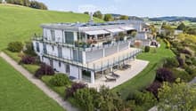 Modern two-story house with large balconies, surrounded by a well-maintained garden and lawn area.