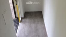 A clean, modern hallway with grey tiled flooring and white walls, featuring a staircase leading upwards and an open doorway to the left.