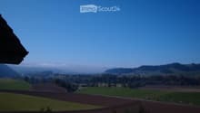Panoramic view of a rural landscape with fields, scattered trees, and distant hills under a clear blue sky.