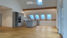 Bright, open kitchen with wooden flooring, modern grey cabinetry, and multiple skylights providing natural light. The space is completely empty, with no furniture or appliances visible.