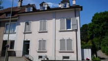 Two-story residential house with light pink facade, multiple windows with shutters, and a small balcony on the first floor.
