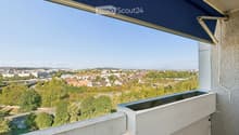 Balcony with a retractable awning, overlooking a cityscape with trees, buildings, and distant mountains.