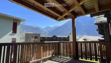 Wooden balcony with a railing, overlooking a scenic mountain view and neighboring houses.