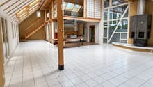 Bright, open room with white tiled flooring, wooden beams, and large windows. The space is empty, with no furniture or furnishings visible.