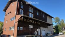 Two-story wooden building with brick and wood siding, multiple windows, balconies, and a sign reading "MÜHLE".
