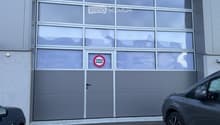 Gray building, large garage doors, 'Passage Interdit' sign, small pedestrian door, yellow parking lines