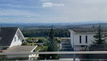 Balcony with metal railing overlooking a suburban area with houses, trees, and distant mountains under a partly cloudy sky.