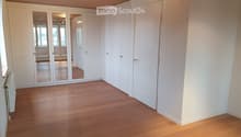 Empty room with light wooden flooring, white walls, and a large mirrored wardrobe unit. The room has a door leading to another space and a radiator on the left side.