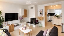 Modern living room with a dark grey sectional sofa, white coffee table, fireplace, flat-screen TV, and decorative plants.