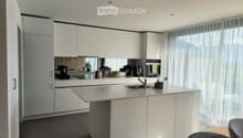 Modern kitchen with white cabinets, a central island, and a sink. Appliances and small items are visible on the counter.