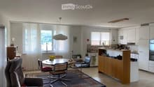Open-plan living and dining area with a sofa, dining table, chairs, and a modern kitchen featuring white cabinets, a counter, and appliances.