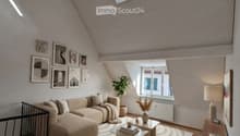 Modern living room with wooden flooring, a large sectional sofa, a glass coffee table, a side table with a lamp, and several picture frames on the wall.