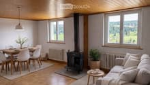 Bright living and dining area with wooden floors, exposed wooden ceiling, large windows offering scenic views, a fireplace, a sofa, a coffee table, a dining table with chairs, and a flower vase on the table.