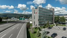 A multi-story office building with the Notz logo on the facade, surrounded by a parking lot and a highway with multiple lanes of traffic.