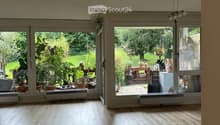Empty room with light wooden flooring, large windows, and sliding glass doors leading to a garden area.