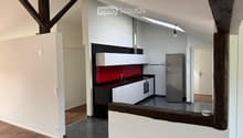 Modern kitchen with white cabinets, stainless steel appliances, and a red backsplash. The space features wooden flooring and exposed wooden beams.