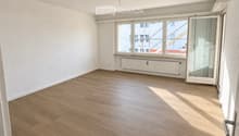 Empty room with wooden flooring, white walls, large windows, and a radiator. No furniture or equipment present.