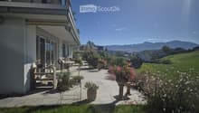 Well-maintained garden with a patio area, outdoor furniture, potted plants, and a scenic mountain view in the background.