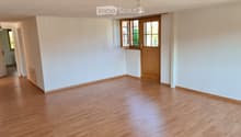 Empty room with light wooden flooring, white walls, and a wooden door leading to another space.