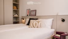 Modern bedroom with a neatly made bed, nightstand, and decorative items on shelves and walls.