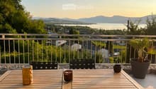 Balcony with wooden table, black chairs, and scenic view of a lake and mountains.