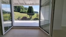 Open sliding glass doors lead to a balcony with a view of a green field and trees.