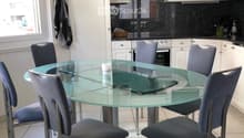 Modern kitchen with white cabinets, a glass dining table surrounded by four grey chairs, and a microwave on the counter.