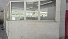 Corner of a building with white brick walls and large windows, showing reflections of parked cars and outdoor area.
