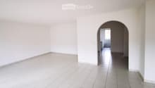 Empty room with white tiled floor and walls, featuring an arched doorway leading to a small bathroom with white tiles and a sink.