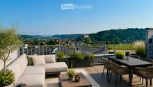 A modern rooftop terrace with a panoramic city view, featuring a cream-colored sofa, a small coffee table, a dining table with four chairs, and several potted plants.