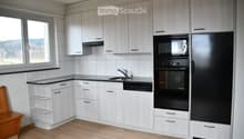 Modern kitchen with white cabinets, black appliances, and a wooden floor. Features a sink, microwave, oven, refrigerator, and dishwasher.