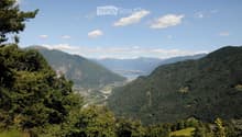 Panoramic mountain view with lush green forests, a lake, and a town nestled in the valley below.