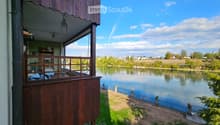 Wooden balcony overlooking a serene river with a scenic view of the surrounding landscape and town.