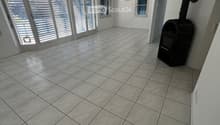 Empty room with tiled floor, large windows with blinds, and a small black stove in the corner.