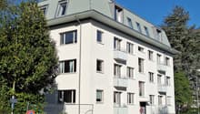 Four-story residential building with white facade, multiple windows, and balconies on the upper floors.