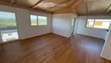 Empty room with wooden flooring, white walls, and large windows offering a scenic view. The ceiling features exposed wooden beams.