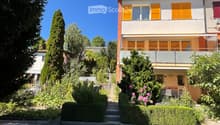 Two-story house with yellow shutters, balcony, garden, and steps leading to the entrance.