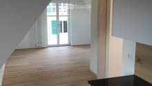 An unfurnished attic room with wooden flooring, white walls, and a sliding glass door leading to a balcony.
